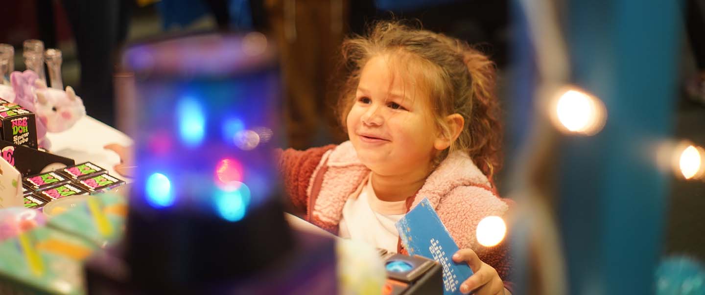 Young girl smiles while holding a Science Museum Oklahoma souvenir at the museum gift shop at the Winter WonderLab event.