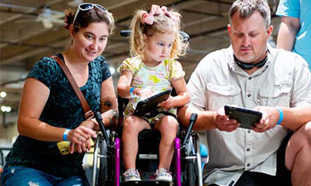 A family explores robotics at Science Museum Oklahoma, with a young girl in a wheelchair using a tablet to program robots in an inclusive STEM learning environment.