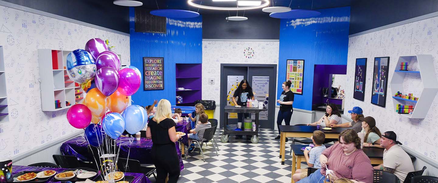 Families celebrate a child’s birthday in a private party room at Science Museum Oklahoma with pizza, balloons, and a live science demonstration led by museum staff.