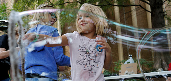 A child plays with giant bubbles during an outdoor science activity at Science Museum Oklahoma, experiencing hands-on STEM fun in the museum’s gardens.