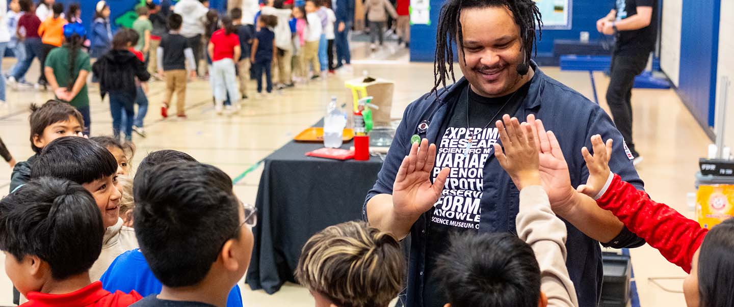 Science Museum Oklahoma educator high-fives elementary school students during a STEAM outreach program.