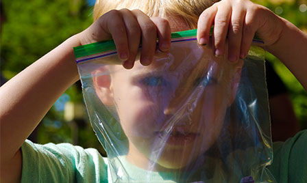 Young boy looking through a plastic bag while waiting to participate in an outdoor project in the gardens of Science Museum Oklahoma.